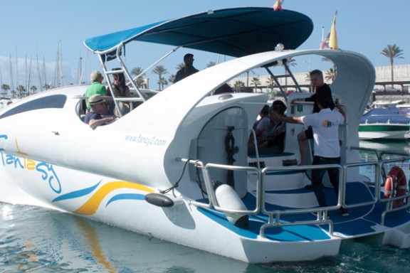 Futuristic boat with blue and yellow design docked at a marina.