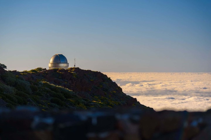 Observatory dome on hill above a sea of clouds at sunset.