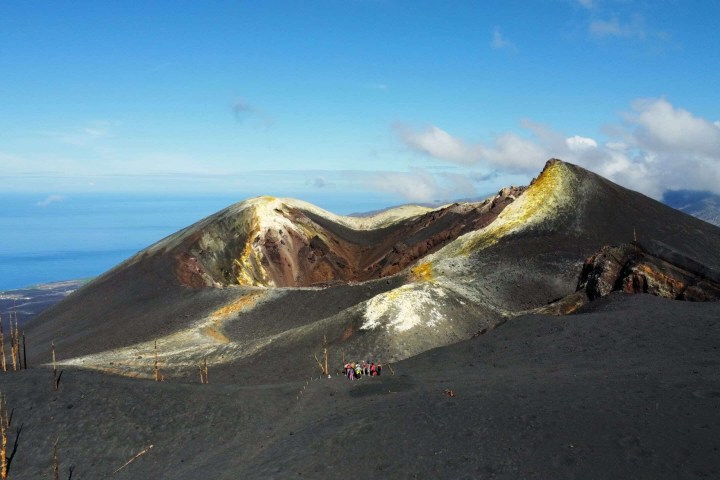 Group of hikers on a volcanic landscape with distant ocean view.