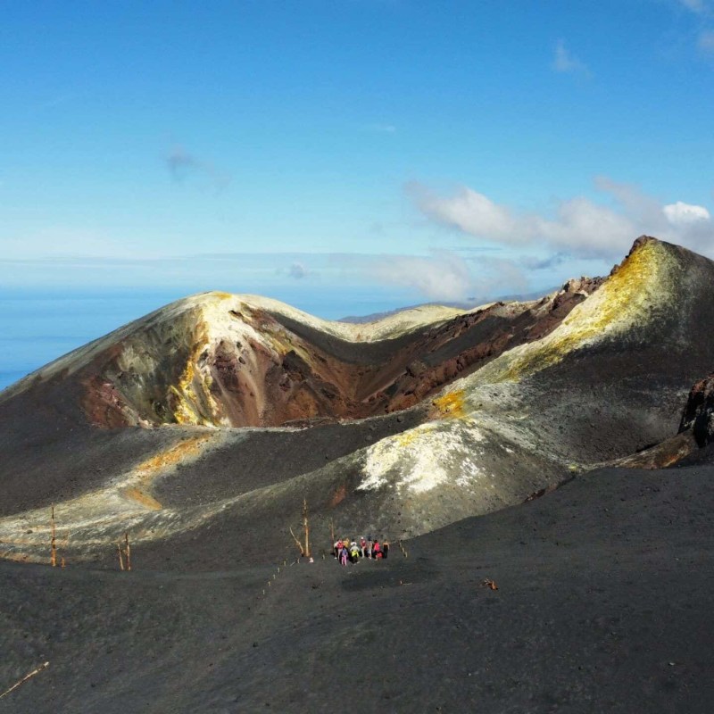 Group of hikers on a volcanic landscape with distant ocean view.