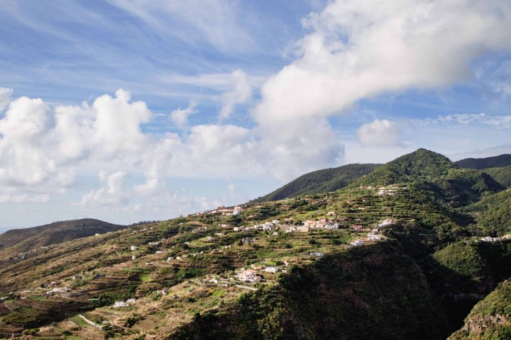 Hillside village with lush greenery under a partly cloudy sky.