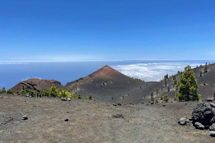 Mountain landscape with volcanic terrain and distant ocean view under a clear blue sky.