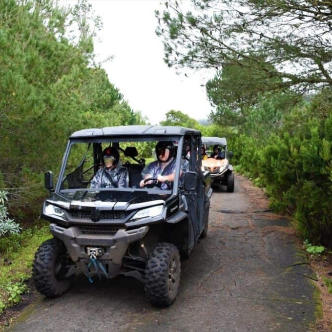 Two off-road vehicles with passengers driving on a forest path.