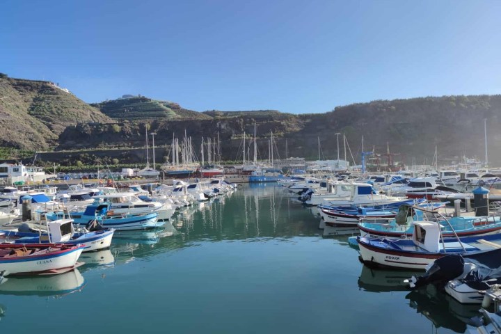 Scenic marina with boats and mountains in the background on a sunny day.
